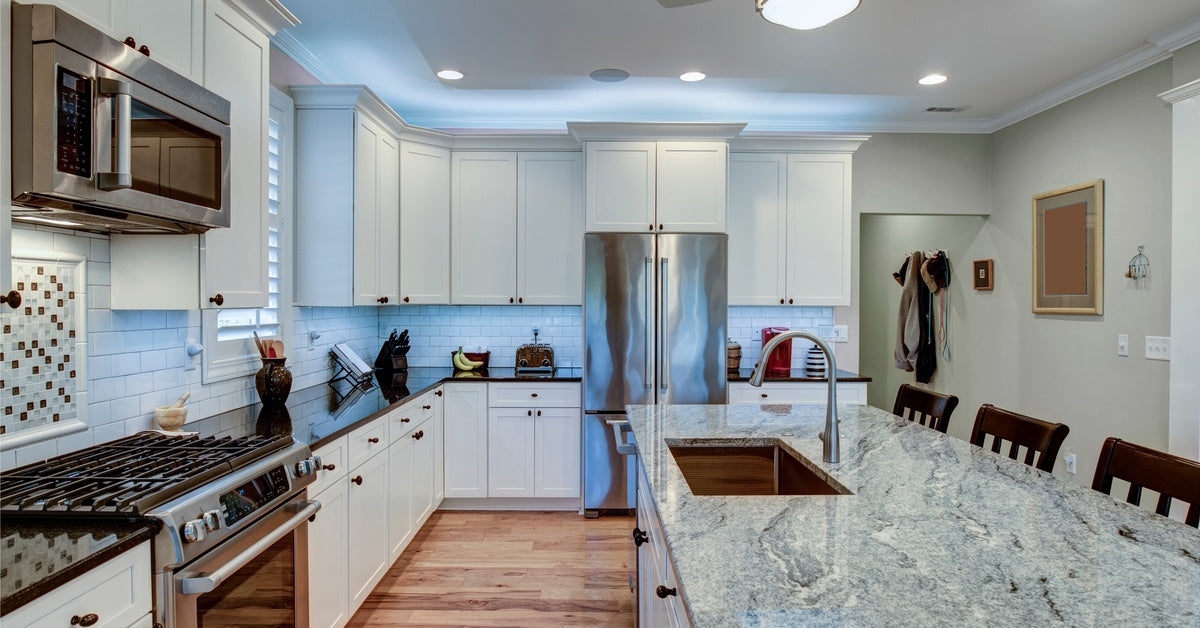 A mostly white kitchen with a large center island with a big slab of granite on it. The sink is in the island.