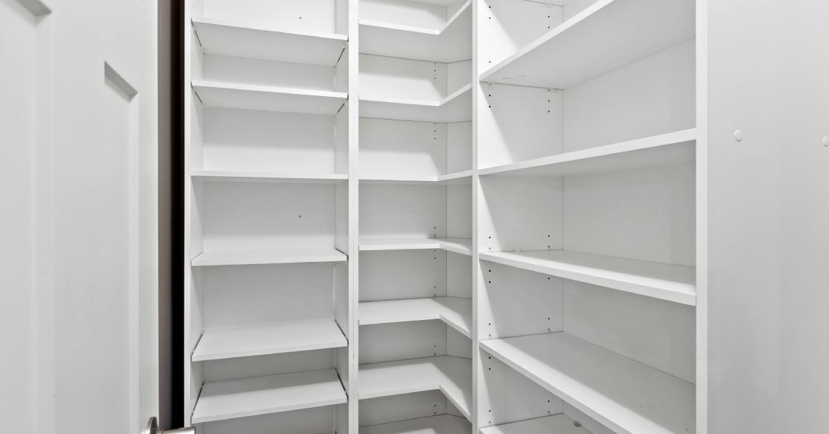 A residential walk-in pantry with empty shelving. The shelving is all white and there's a pantry door on the left.