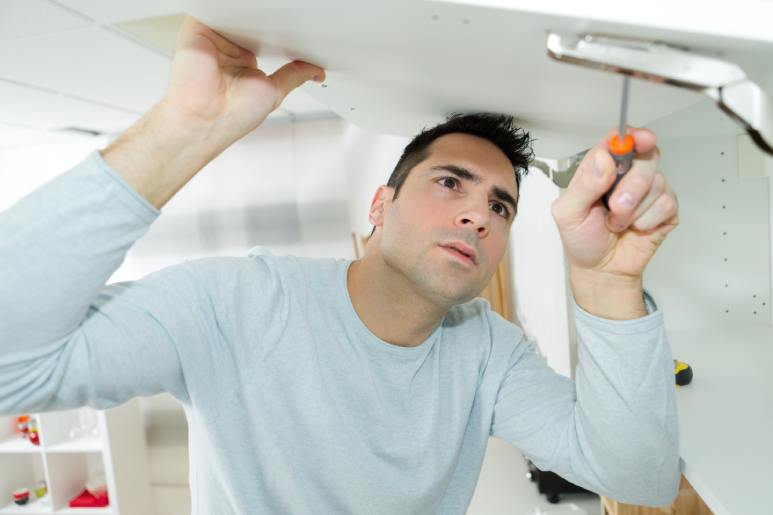 A homeowner tucked underneath a kitchen cabinet door with a screwdriver to adjust the bracket screws.