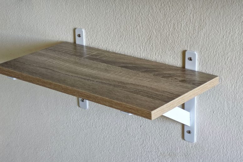 A floating shelf bracket mounted to the wall with white, powder-coated shelf brackets. The shelf is wooden.