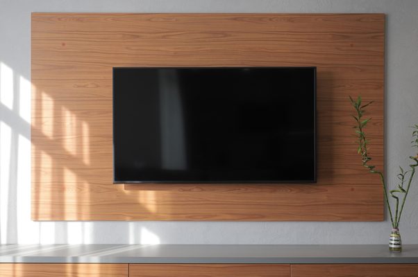 A large flat-screen television installed on a wooden panel on a wall above a matching wooden console.