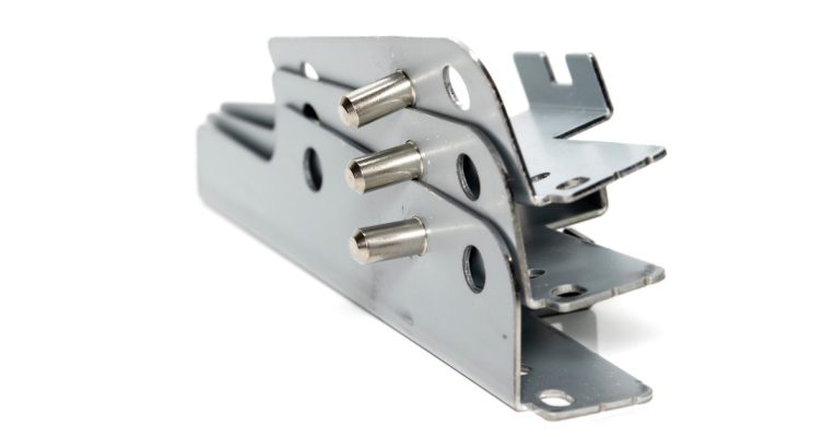 A stack of three metal brackets with stud pins affixed to them. The stack sits against a white background.
