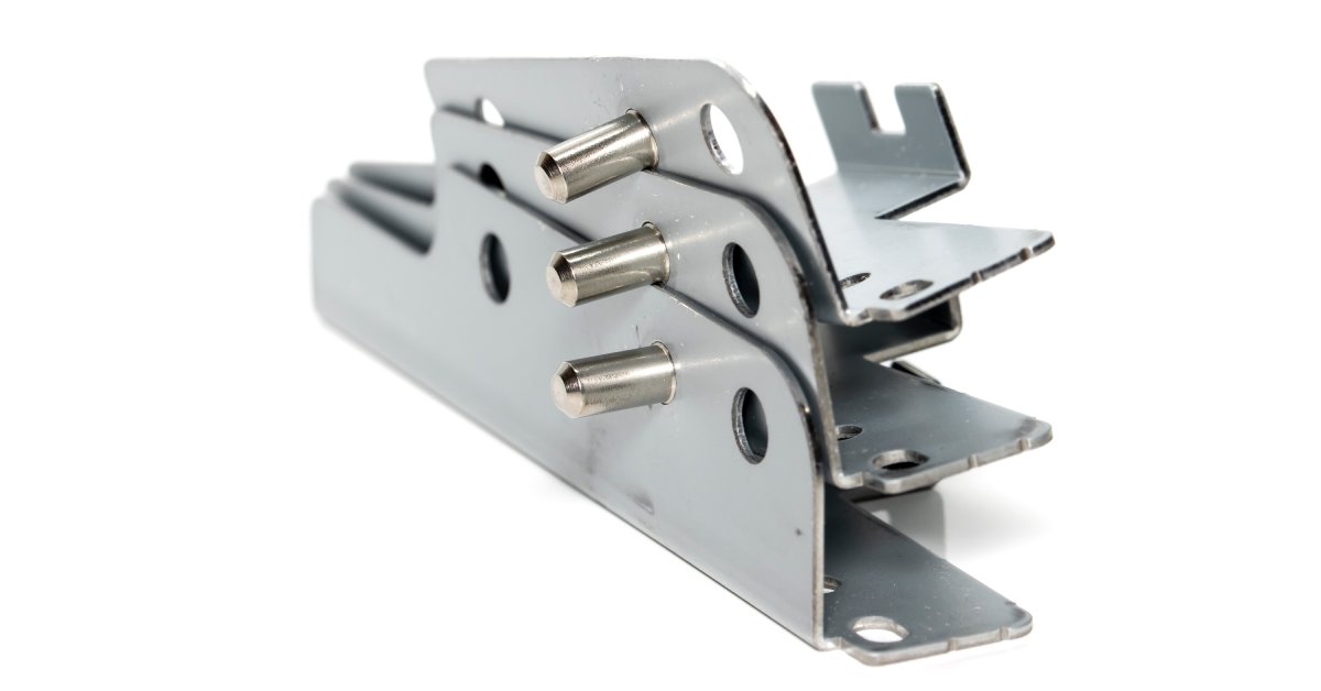 A stack of three metal brackets with stud pins affixed to them. The stack sits against a white background.